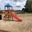 Structure de aire de jeux en bois Climbing Booth avec toit bleu, toboggan rouge et éléments d’escalade dans un san