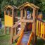 Alpha playhouse with slide sur une aire de jeux herbeuse avec des enfants qui jouent.