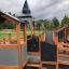 Structure de jeu en bois Campanille playground castle avec toboggans et structures d’escalade dans un parc.