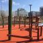 Spillikins wooden playhouse dans une aire de jeux extérieure avec revêtement de sécurité rouge et bâtiments urbains environnants