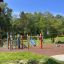 Aire de jeux colorée sur le thème des crayons avec maisonnette en bois et toboggan dans un parc.