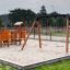 Double Safety Seat double swing sur une aire de jeux sablonneuse avec toboggan et structures d'escalade.