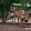 Triangle Modern Nature wooden playhouse with slide dans un parc