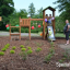 Triangle Modern Nature wooden playhouse with slide dans un parc avec des enfants qui jouent.