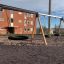 Triple swing avec sièges en pneu dans une aire de jeux devant un bâtiment en briques.