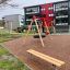 Bench, Steel Construction dans une aire de jeux avec portique de balançoires et immeubles résidentiels en arrière-plan.