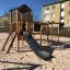 Aire de jeux en bois Romping Cottage avec toboggan et éléments d’escalade.