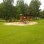 Ensemble d’aire de jeux en bois Romping Cottage avec toboggan et balançoires dans un parc verdoyant