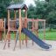 Structure de jeu en bois Romping Cottage avec toboggan et filet d’escalade.