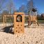 Structure de jeu en bois Romping Cottage avec mur d’escalade et sol en sable.