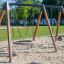Swing Frame 1(BNS) +1 (double swing) sur une aire de jeux sablonneuse avec un siège circulaire.