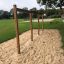 Structure en bois Rope Bar dans une aire de jeux avec de l’herbe et du sable autour.