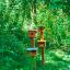 Poteaux de mangeoires à oiseaux en bois installés dans une pelouse verte près de bâtiments modernes.