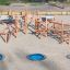 Structure d’escalade en bois Sonora avec trois trampolines bleus enterrés dans une aire de jeux sablonneuse