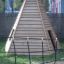 Ural climbing net devant une structure pyramidale en bois dans une aire de jeux.
