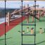 Ural climbing net sur une aire de jeux extérieure avec des structures en bois à l’arrière-plan.