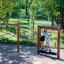 Enfants jouant sur un équipement de jeu Trim Trail Nature II en bois pour grimper et s’équilibrer dans une aire de jeux
