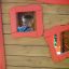 Enfant regardant dehors depuis l’intérieur d’une structure en bois Anna's Playhouse avec cadres rouges.