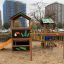 Jungle House playhouse with slide dans une aire de jeux avec des immeubles en arrière-plan.