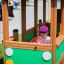 Un enfant joue à l’intérieur d’un équipement de jeu Bus en bois vert.