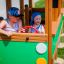 Des enfants jouent dans une structure Bus en bois dans une aire de jeux.