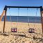 Double Baby Swing installé sur une plage de sable avec vue sur la mer.
