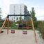 Double Baby Swing avec structure en bois et sièges rouges et bleus dans une aire de jeux urbaine