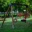 Un Double Swing en bois installé sur une aire de jeux verte.