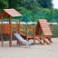 Galapagos wooden playhouse with slide dans une aire de jeux sablonneuse.