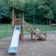 Elbrus wooden playhouse with slide dans une aire de jeux entourée d’arbres