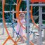 Enfant grimpant sur une structure de jeu Ursa Maior orange et bleue avec toboggan et filet d’escalade