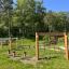 Structure de jeu extérieure en bois 'Obstacle course' dans un parc verdoyant avec filets d’escalade et poutres d’équilibre.