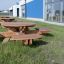 Round table & benches dans une zone extérieure herbeuse près d’un bâtiment moderne.