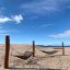 Double Hammock sur une plage de sable avec des supports en bois et un ciel bleu clair.