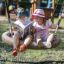 Deux enfants assis sur un Bird Nest Single Swing (BNS 120 cm) lisant un livre dans une aire de jeux.