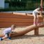 Des enfants jouent sur la poutre d’équilibre en bois Ramp dans une aire de jeux extérieure.