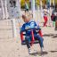 Un enfant joue sur un Nature Double Swing dans une aire de jeux sablonneuse.