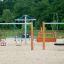 Nature Double Swing sur une aire de jeux sablonneuse avec des arbres en arrière-plan.