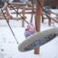 Un enfant joue sur la balançoire simple dans une aire de jeux enneigée.