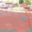 Rouge Cross Climber steel structure sur une aire de jeux avec des tapis de sécurité.