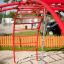Rouge Cross Climber steel structure sur une aire de jeux avec du sable et une corde suspendue.