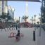 Des enfants jouent sur un Double Seesaw rouge dans une aire de jeux urbaine moderne.
