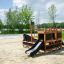 Structure de jeu en bois Small Ship Nature avec toboggan sur sol sablonneux dans un parc.