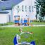 Bird swing rocking sur une aire de jeux herbeuse devant un bâtiment blanc