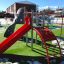 Aire de jeux Whale - AZTEC steel structure avec toboggan rouge et murs d'escalade sur une pelouse verte.