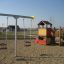 Baby Double Swing dans une aire de jeux avec une maisonnette et une structure d’escalade.