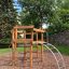Sherwood wooden playhouse dans un parc avec des arbres et un mur en pierre à l'arrière-plan.