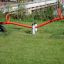 Seesaw rouge sur une aire de jeux herbeuse avec support en pneu noir.