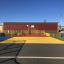 Terrain de sport multicolore Maracana avec panier de basket, entouré de clôtures jaunes.