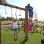 Des enfants jouent sur la structure de jeu Alv avec des poteaux en bois, des cordes d'escalade et une arche métallique en dessous
